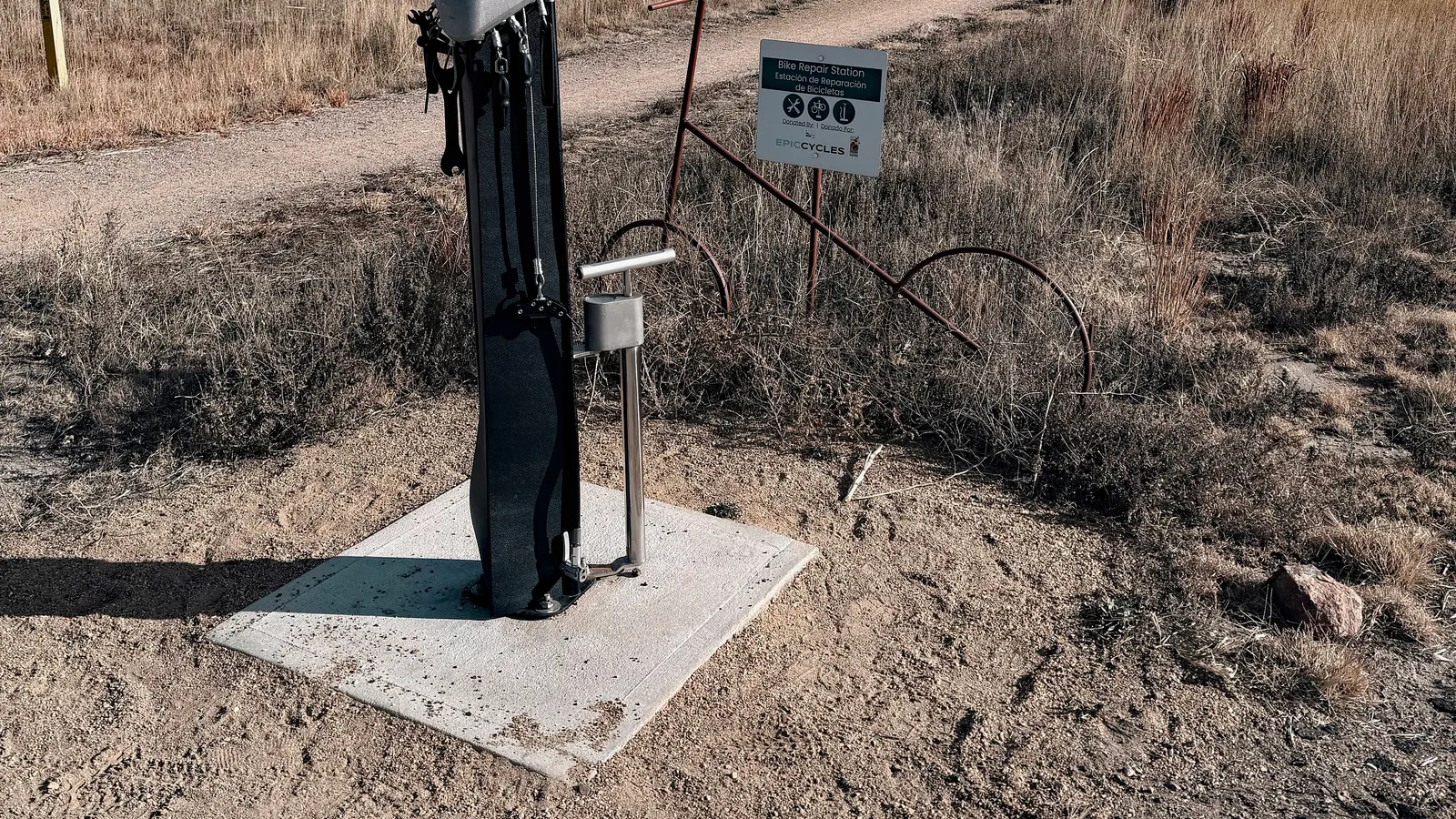 Borne de réparation de vélo en bord de chemin, avec pompe et outils attachés à un support noir